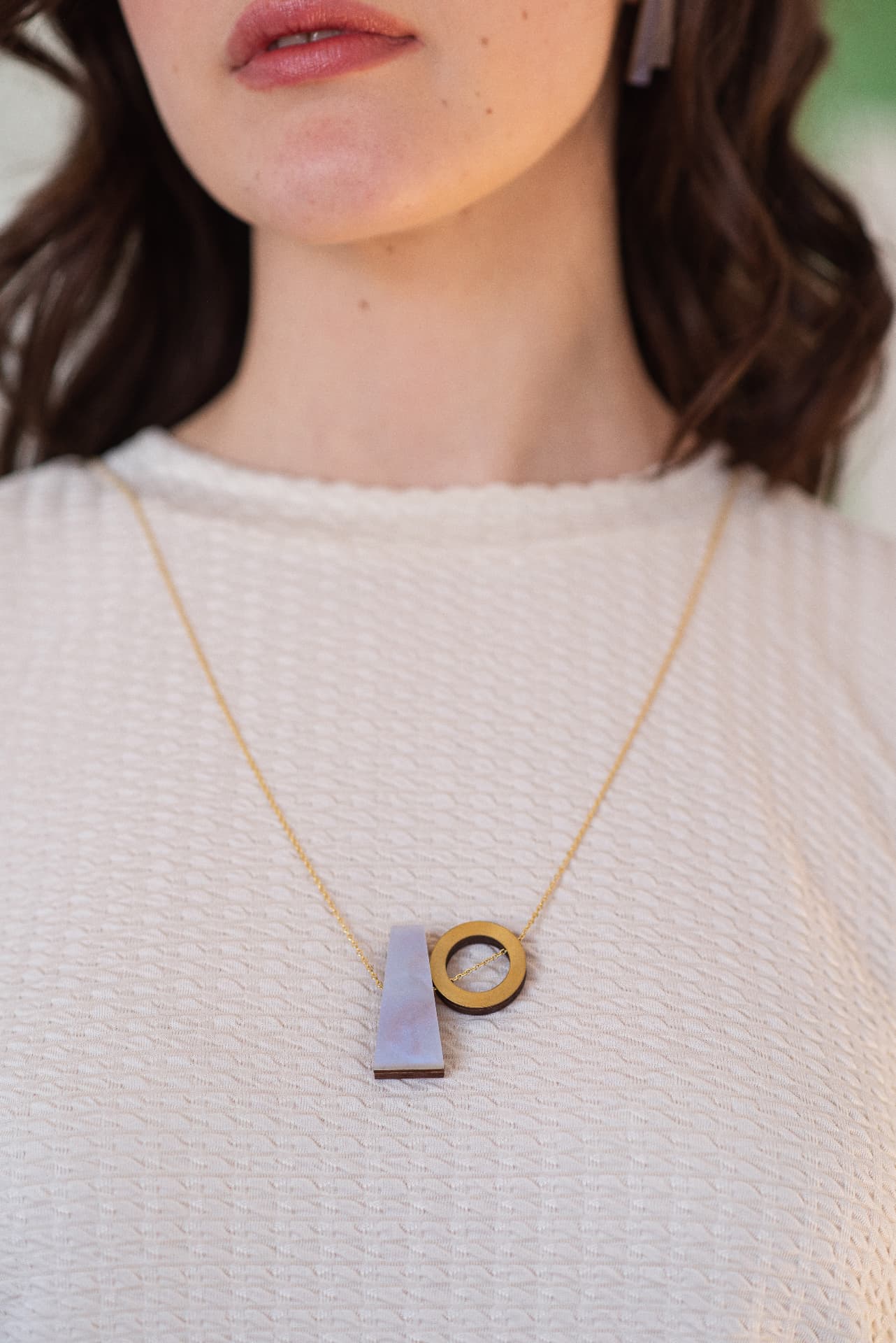 Model wearing a geometric plywood pendant necklace in lilac and brass